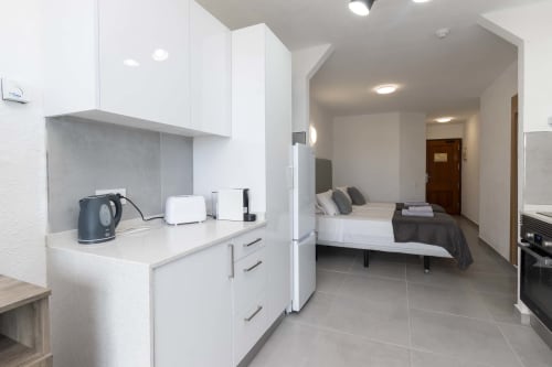 Modern studio apartment kitchenette and bedroom in Costa Adeje, Tenerife with white cabinetry, stainless steel appliances,