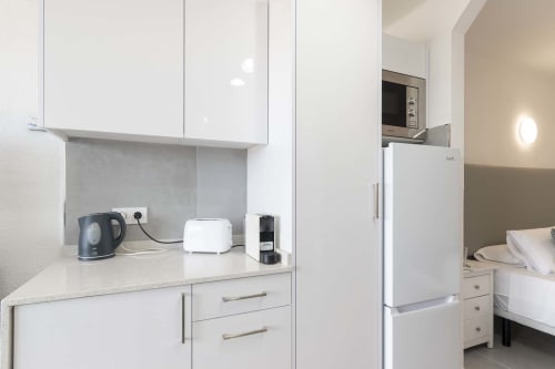 Modern studio kitchenette in Costa Adeje apartment with white cabinetry, kettle, toaster, coffee maker, and refrigerator
