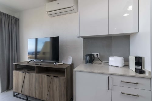 Modern studio kitchenette and entertainment area with flat-screen TV, white cabinetry, and sea view in Costa Adeje