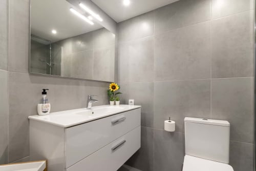 Modern bathroom in Costa Adeje studio apartment with white vanity, large mirror, toilet, and sunflower decor