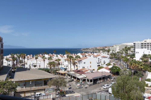 Aerial view of Costa Adeje, Tenerife resort with white apartments, palm trees, ocean, and beachfront street