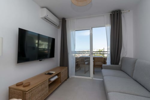 Modern studio apartment in Costa Adeje, Tenerife with gray sofa, wall-mounted TV, wooden dresser, and sea view balcony