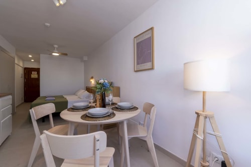 Modern studio dining area in Costa Adeje with round table, white chairs, lamp, and bed visible in contemporary apartment