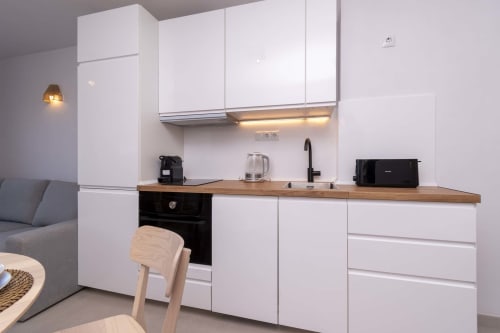 Modern refurbished studio kitchen in Costa Adeje, Tenerife with white cabinets, wooden countertop, and black oven appliances