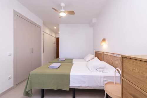 Modern refurbished studio bedroom in Costa Adeje, Tenerife with twin beds, ceiling fan, wooden furniture and white walls
