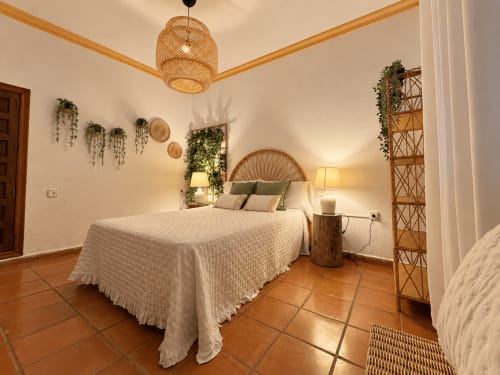 Dormitorio de lujo en Casa Rural Garden Suites en Xàtiva con lámpara de mimbre tejido, cabecero de ratán, plantas en maceta y