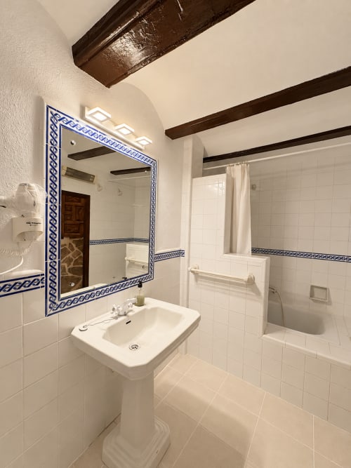 Baño moderno con azulejos blancos, espejo con marco azul, lavabo de pedestal y ducha en Casa Rural Garden Suites, Xàtiva