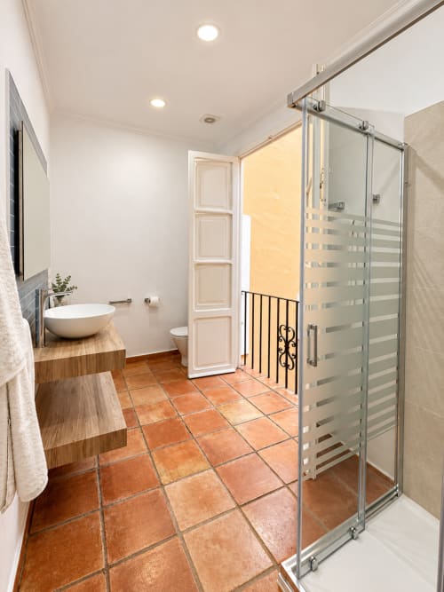 Baño moderno en Casa Rural Garden Suites, Xàtiva, con ducha de cristal, lavabo redondo, suelo de baldosa de barro y acceso a balcón