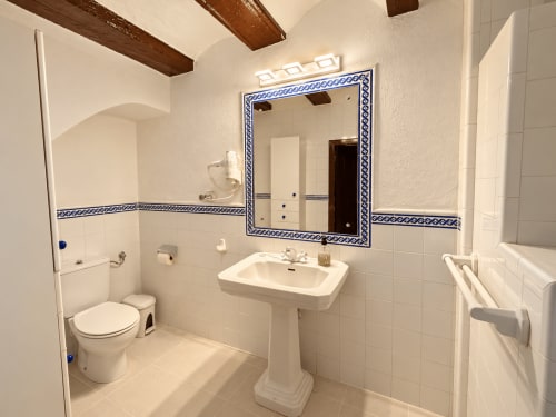 Baño de la suite deluxe de Casa Rural Garden Suites con lavabo pedestal, espejo con marco azul, inodoro y paredes de azulejos blancos