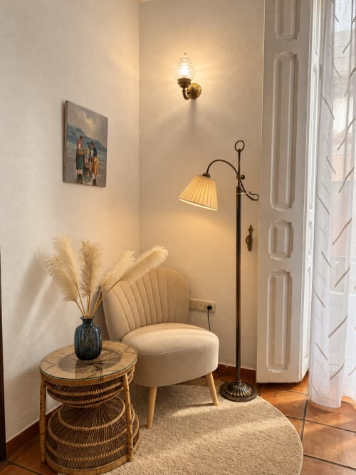 Acogedor rincón de descanso en Casa Rural Garden Suites de Xàtiva con sillón crema, mesita tejida y lámpara de pie vintage