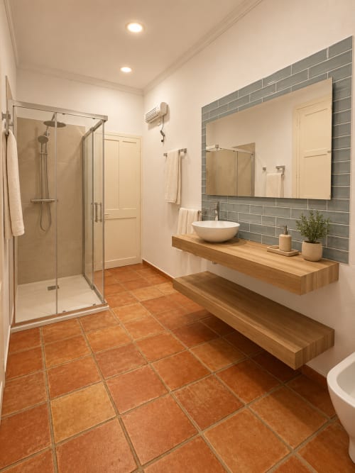 Baño moderno con piso de baldosas terracota, tocador flotante de madera con lavamanos blanco tipo recipiente, backsplash de baldosas grises, espejo, y