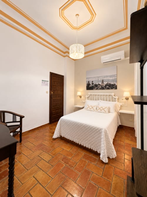 Elegante dormitorio en Casa Rural Garden Suites en Xàtiva con cama blanca, suelo de baldosas de barro y techo dorado decorativo