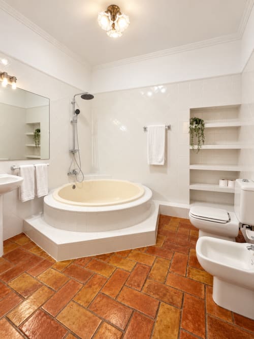 Lujoso cuarto de baño en Casa Rural Garden Suites de Xàtiva con bañera redonda, suelo de baldosa terracota y paredes de azulejos blancos