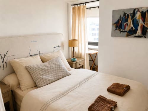 Chambre lumineuse de l'appartement Les Maraîchades au Cap Ferret avec literie crème, tête de lit décor nautique et ambiance côtière