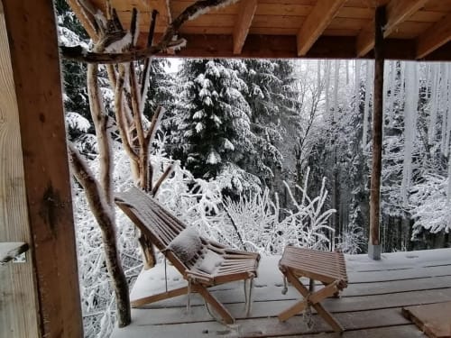 Porche enneigé en hiver à la Furanelle B&B à Saint-Étienne, avec des chaises en bois et vue sur la forêt