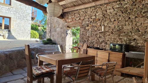 Terrasse en pierre rustique de la maison d'hôtes Furanelle à Saint-Étienne avec table à manger, chaises en bois et cuisine
