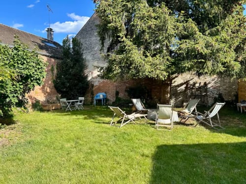 Cour de jardin du gîte Les Maraîchades en Sologne avec chaises longues, pelouse et murs de pierre couverts de lierre