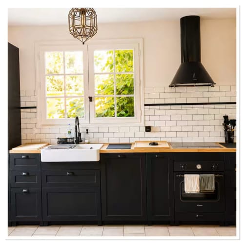 Cuisine moderne noire avec carrelage métro blanc, comptoirs en bois naturel et vue sur le jardin du gîte Les Maraîchades