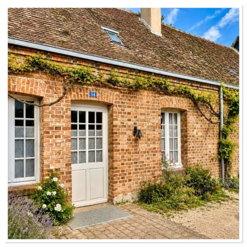 Entrée pittoresque du gîte Les Maraîchades en Sologne : porte crème, murs de briques couverts de lierre et fleurs du jardin