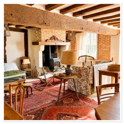 Intérieur rustique du cottage Les Maraîchades avec poutres apparentes, cheminée en brique, mobilier d'époque et tapis orientaux rouges