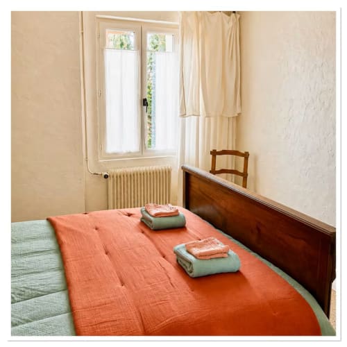 Chambre douillette du gîte Les Maraîchades en Sologne avec dessus-de-lit orange, lit en bois et vue sur le jardin