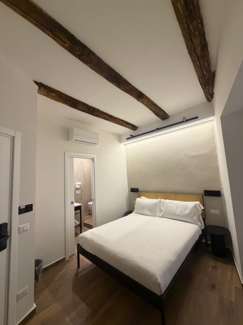 Camera moderna in un lussuoso B&B a Napoli con travi in legno a vista, letto queen con biancheria bianca e design minimalista