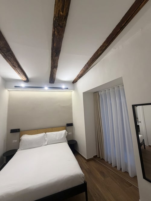 Camera moderna al Salotto Toledo con travi in legno a vista, biancheria bianca e vista sulla città di Napoli