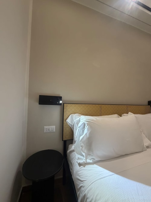 Camera d'hotel a Salotto Toledo con cuscini bianchi, testata in rattan, comodino e unità AC murale a Napoli