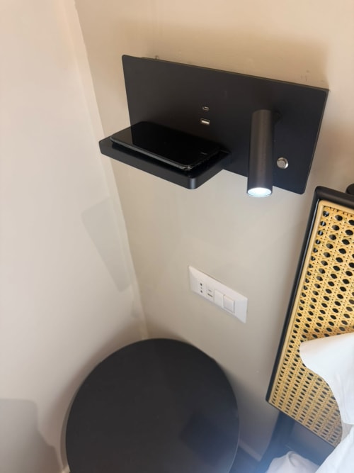 Mensola nera a parete con smartphone e lampada da lettura nella suite Salotto Toledo, Napoli