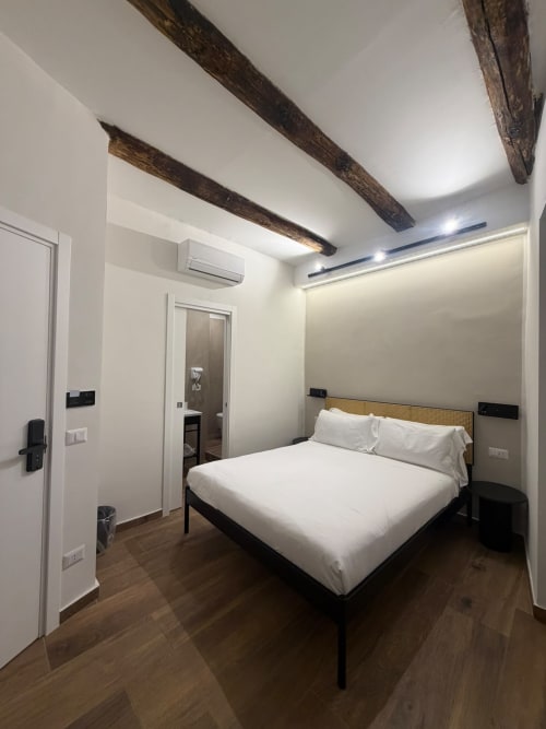 Camera moderna nel lussuoso hotel Salotto Toledo a Napoli con letto queen, travi a vista, pareti bianche, pavimenti in legno e vista sulla città