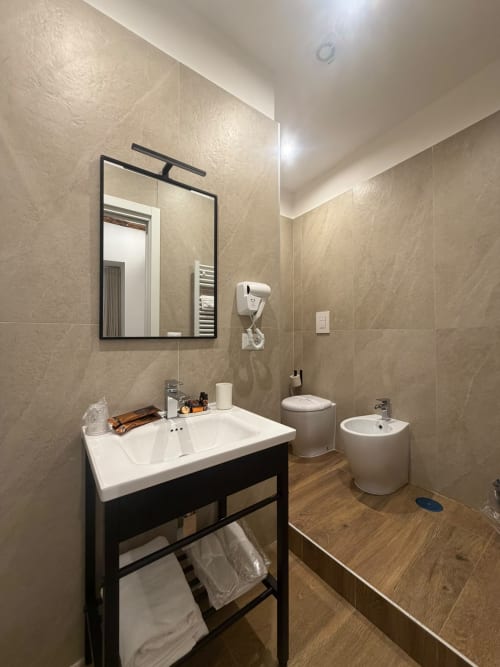 Bagno moderno al Salotto Toledo, lussuoso B&B a Napoli, con lavabo bianco, mobile nero, bidet e pareti rivestite in piastrelle beige