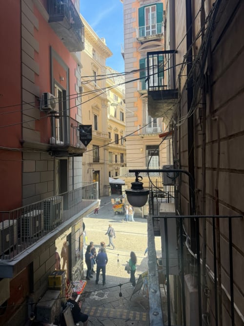 Stretta via napoletana con edifici storici colorati, passanti e lampione, vista dalla lussuosa suite Salotto Toledo