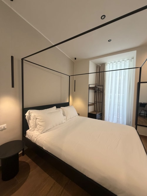 Camera da letto moderna con letto a quattro colonne nero e biancheria bianca presso l'hotel di lusso Salotto Toledo a Napoli, Italia