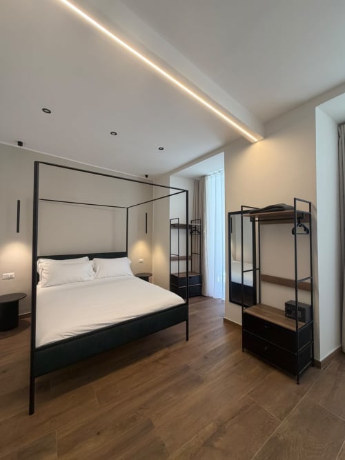 Camera da letto di lusso moderno presso Salotto Toledo Napoli con letto a baldacchino nero, biancheria bianca, pavimenti in legno e illuminazione contemporanea