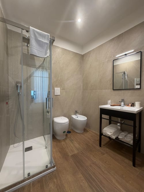 Bagno moderno nella suite di lusso Salotto Toledo a Napoli, con doccia in vetro, wc, bidet e lavabo nero con specchio