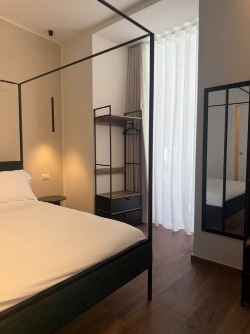 Camera da letto di lusso moderno al Salotto Toledo con letto a quattro colonne nero, tende bianche trasparenti e vista sulla città di Napoli