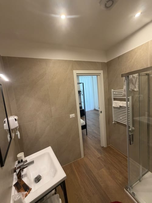 Bagno moderno con ampia doccia, lavandino bianco, scaldasalviette e pavimento effetto legno al Salotto Toledo Napoli di lusso