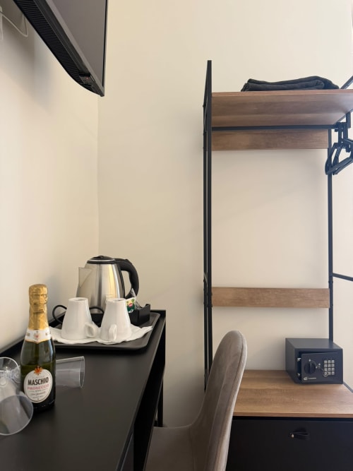 Scrivania di camera d'hotel con bottiglia di Prosecco, bollitore, tazze bianche e cassaforte nella suite Salotto Toledo lusso, Napoli