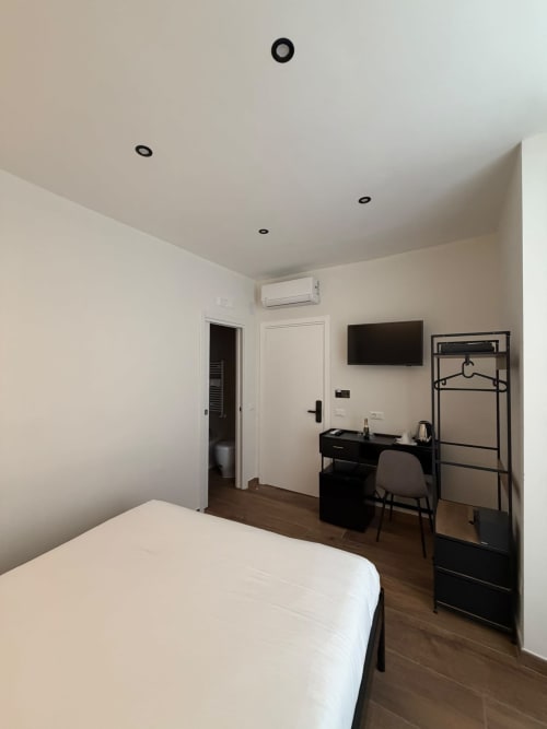 Camera da letto moderna all'hotel Salotto Toledo Napoli con letto bianco, scrivania nera, TV a parete e luci incassate nel soffitto