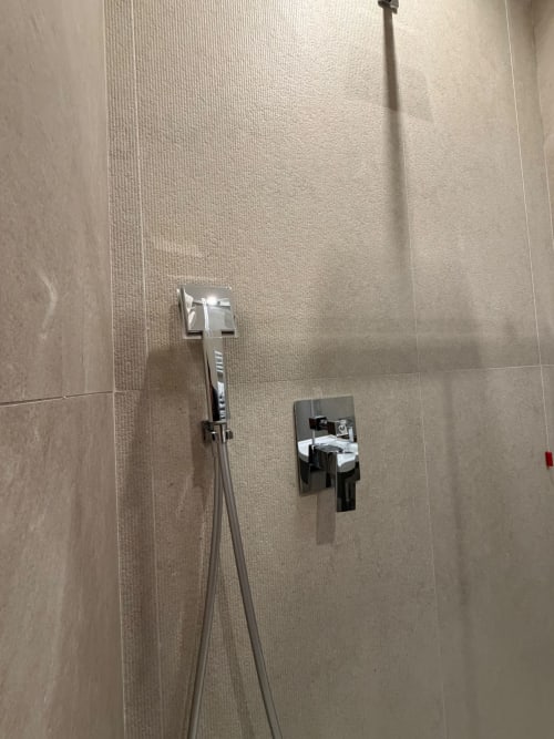 Rubinetteria moderna per doccia e valvola su parete piastrellata beige nel bagno della suite Salotto Toledo, Napoli