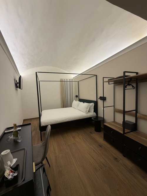 Camera d'hotel moderna presso il Salotto Toledo Napoli con letto a baldacchino nero, pavimenti in legno, scrivania e design minimalista