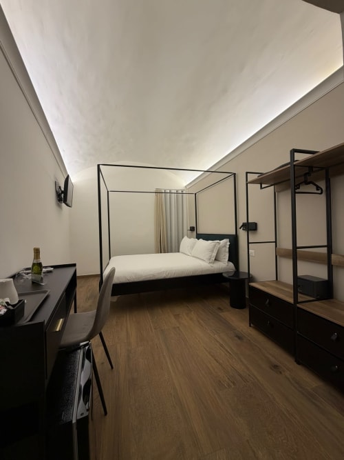 Camera superiore moderna al Salotto Toledo Napoli con letto a baldacchino, scrivania, armadio con cornice nera e pavimenti in legno