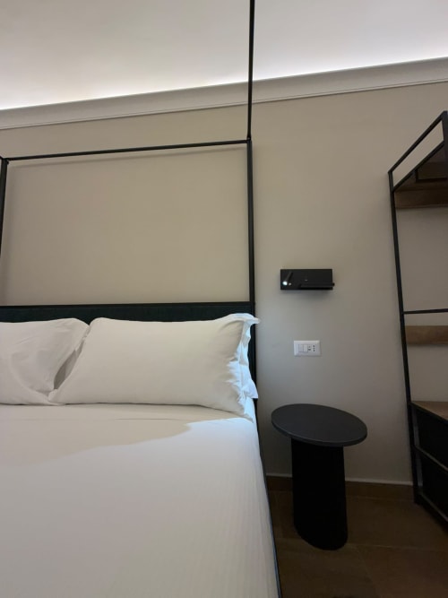 Letto a baldacchino moderno con biancheria bianca e tavolino nero nella suite Salotto Toledo, Napoli