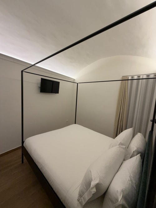 Letto a baldacchino moderno con biancheria bianca nella suite Salotto Toledo lussuosa, Napoli, con TV schermo piatto e stile minimalista elegante
