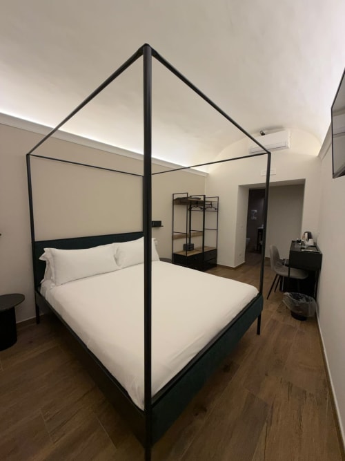 Letto a quattro colonne con struttura nera e biancheria bianca nella camera di lusso Salotto Toledo, Napoli