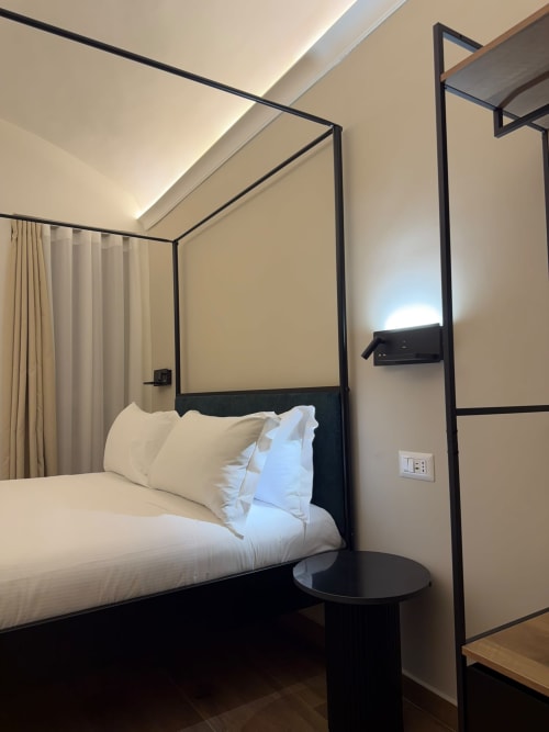 Lussuoso letto a baldacchino con biancheria e cuscini bianchi con struttura in metallo nero nella camera di hotel moderno a Napoli