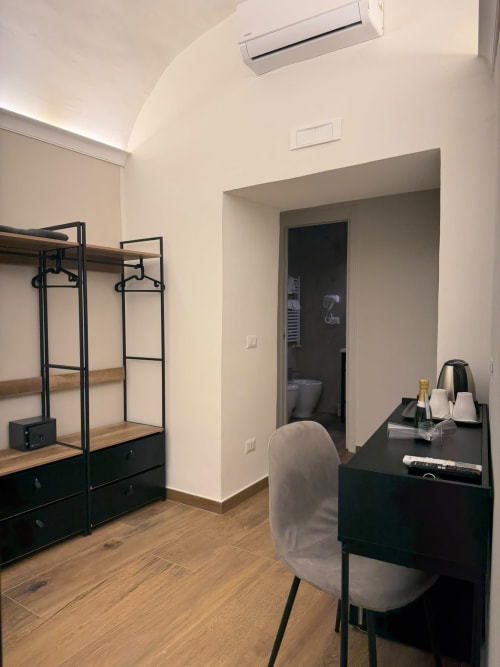 Camera moderna a Salotto Toledo Napoli con scaffali metallici neri, scrivania, sedia, pavimento in legno, climatizzatore e bagno privato