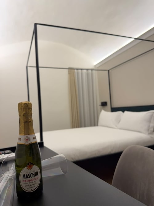 Bottiglia di Prosecco Maschio sulla scrivania in una camera d'hotel di lusso a Napoli con letto a baldacchino e biancheria bianca