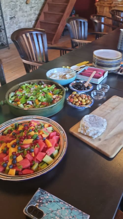 Eettafel in La Fougeraie met kleurrijke frukt- en groenteschalen, kaasplankje en gedekte plaatsen voor gasten