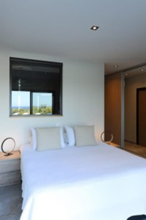 Chambre moderne à la Villa Poggioli à Zonza avec vue mer, literie bleu clair, fenêtre à cadre noir donnant sur le paysage
